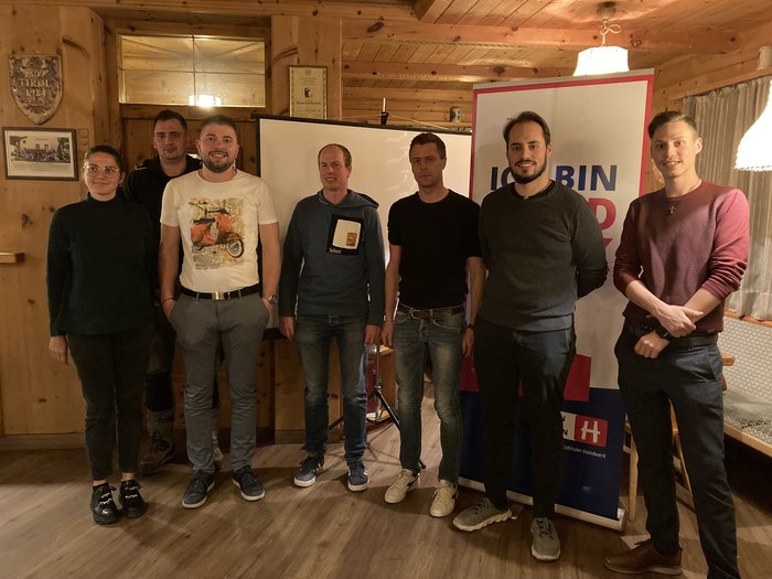 Junghandwerker übernimmt in St. Leonhard in Passeier Sieben Personen in einem Raum mit Holzwänden vor Projektor und Werbebanner