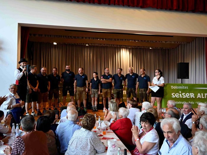 Gli Artigiani Anziani si sono incontrati a Siusi allo Sciliar Gruppo di persone sul palco durante un evento con pubblico che applaude