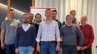 News Gruppenfoto von neun Männern vor einem hellen Vorhang