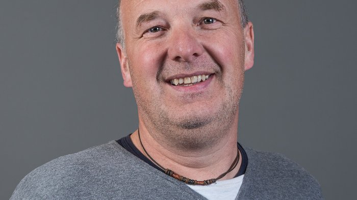 Eisacktaler Wirtschaftsschau kehrt zurück - ein Schaufenster der Vielfalt Lächelnder Mann mit grauem Pullover vor grauem Hintergrund