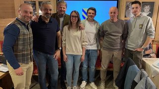 News Sieben Personen posieren vor einem Bildschirm mit Wappen in einem Raum mit Pokalen