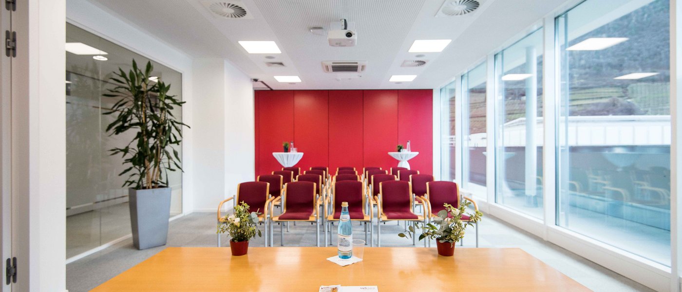 Vermietung Seminarräume Konferenzraum mit roten Stühlen, Tisch und großen Fenstern