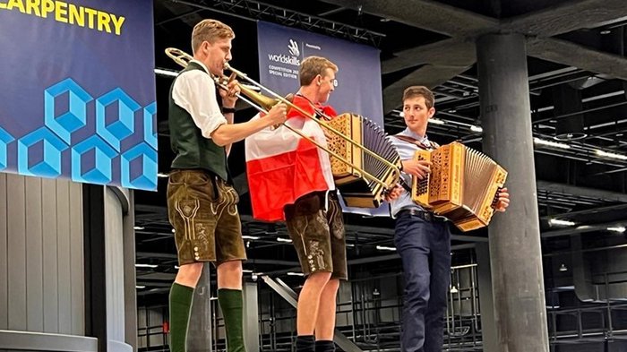 WorldSkills 2022 Special Edition: Zimmerer Marcel Bolego holt Silbermedaille Drei Musiker in traditioneller Kleidung spielen auf einem Holzpodest
