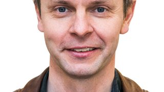 News Porträt eines lächelnden Mannes mit brauner Lederjacke vor weißem Hintergrund