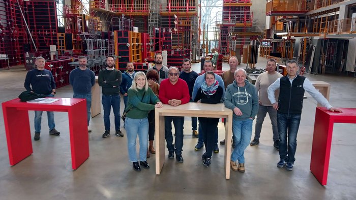 „Die Zukunft des Baugewerbes liegt in der Digitalisierung.“ Gruppe von Menschen in Lagerhalle mit Regalgestellen und Tischen