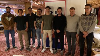 News Acht Männer stehen in einem Raum mit rotem Teppich und Holzbalken an der Decke