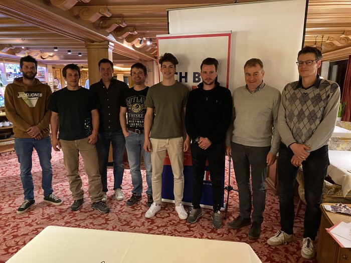 Auf jung folgt jung Acht Männer stehen in einem Raum mit rotem Teppich und Holzbalken an der Decke