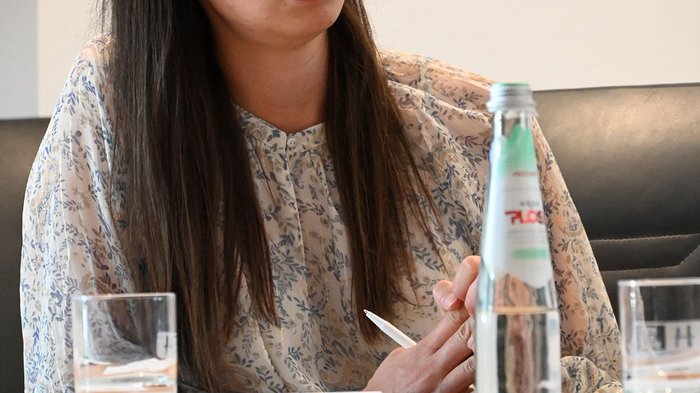 Wohnen muss leistbar sein! Herausforderungen und Lösungsansätze in Südtirol Frau sitzt am Tisch mit Flasche Wasser und Glas und schreibt Notizen