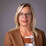 Das lvh-Team Porträt einer Frau mit Brille, blondem Haar und braunem Blazer vor grauem Hintergrund