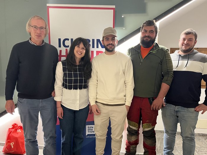 Nuovo slancio per l'artigianato Cinque persone sorridenti in piedi davanti a un cartello con scritte in un edificio