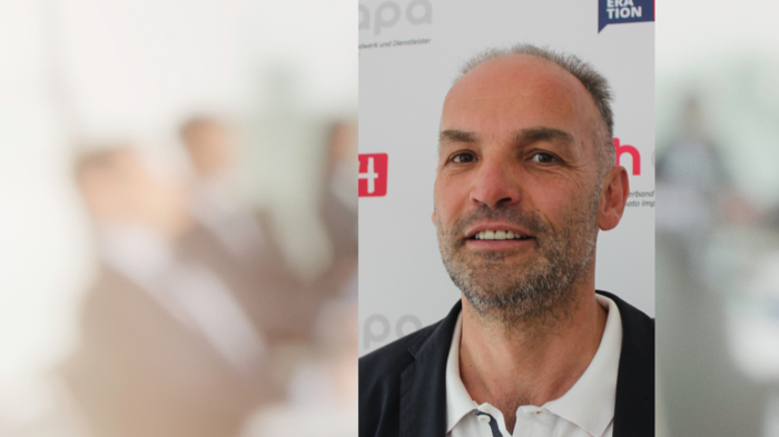 Brennerachse: Warentransporteurinnen und -transporteure im lvh begrüßen Entscheidung der EU Porträt eines lächelnden Mannes vor einem Werbeplakat mit Text