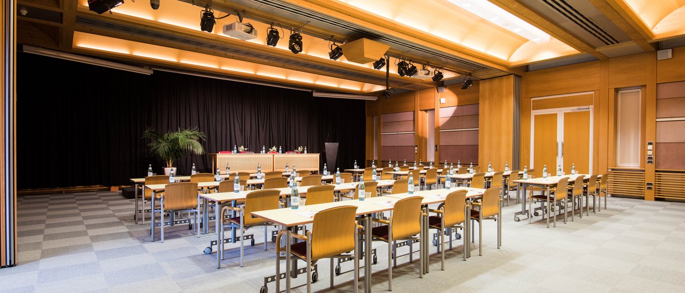 Vermietung Seminarräume Konferenzraum mit Tischen und Stühlen, Flaschen und Bühne mit schwarzem Vorhang