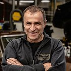 Carrozzieri Uomo sorridente con giacca nera e braccia incrociate in officina