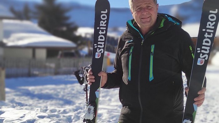 Ein besonderes Weihnachtsgeschenk für Norbert Rier Mann mit grüner Skihose hält zwei Skier im Schnee bei sonnigem Wetter