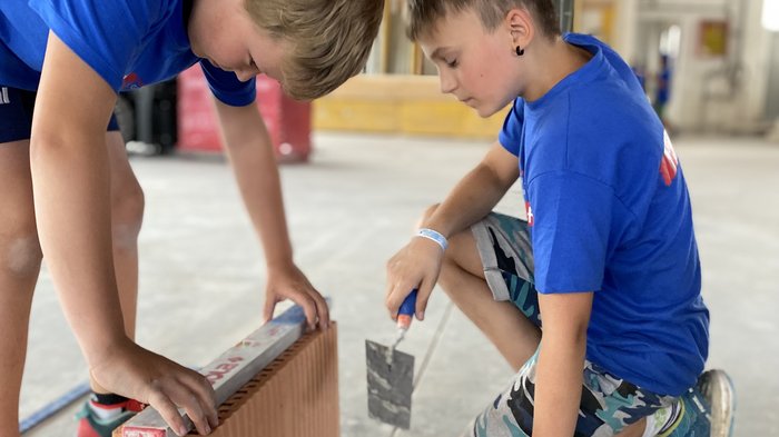 Bild 2: Interessiert und geschickt am Werk während der Projektwoche „Fleißige Baumeister“ © lvh.apa Zwei Jungen arbeiten gemeinsam an einer Mauer mit Kelle und Ziegelstein