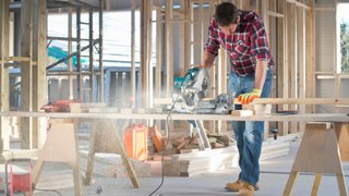 News Mann sägt Holz mit Kappsäge in Baustelle mit offenem Holzrahmen