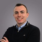 dott.mag. Hannes Zuech Porträt eines lächelnden jungen Mannes vor grauem Hintergrund
