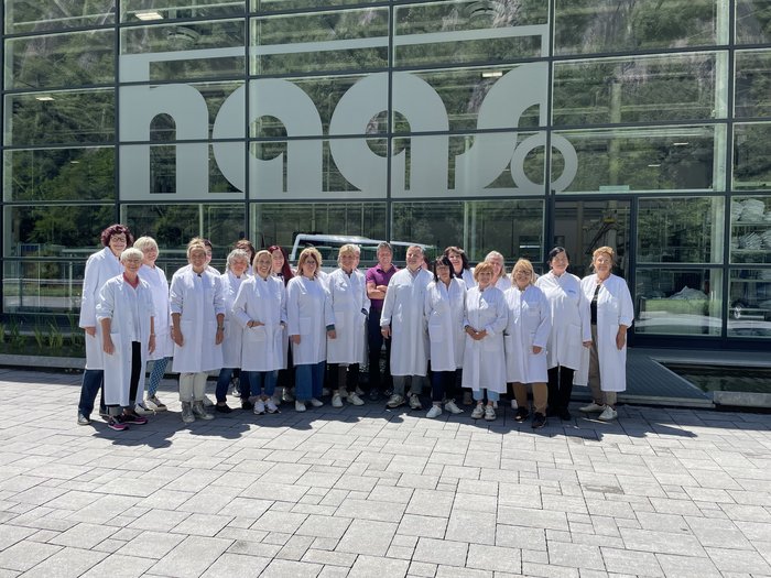 Innovative Einblicke für die Handwerkerfrauen aus dem Oberpustertal Gruppenfoto von Mitarbeitenden in weißen Kitteln vor einem großen Firmenfenster