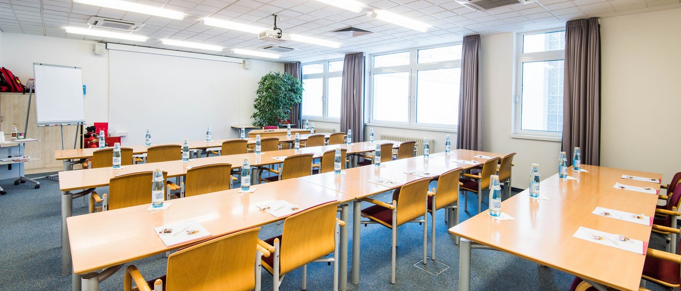 Vermietung Seminarräume Heller Konferenzraum mit Holzstühlen, Tischen, Wasserflaschen und Flipchart