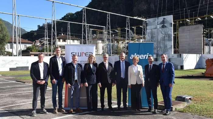 lvh.apa accoglie favorevolmente il programma di investimenti da 500 milioni di euro per Bolzano Nove persone davanti a una struttura di cantiere con banner e montagne boscose sullo sfondo
