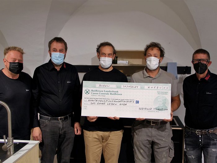 Betriebsbrand: Tischler spenden über 10.000 Euro Fünf Männer mit Masken halten einen großen Scheck in einem Raum