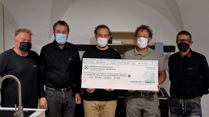 Betriebsbrand: Tischler spenden über 10.000 Euro Fünf Männer mit Masken halten einen großen Scheck in einem Raum