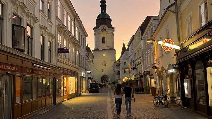 Althandwerker/innen unterwegs: Rundfahrt Weinviertel Paar geht bei Sonnenuntergang durch eine gepflasterte Altstadtstraße mit Uhrturm