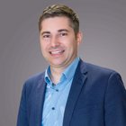 Kernthemen 2024 Porträt eines lächelnden Mannes in blauem Hemd und dunklem Sakko vor grauem Hintergrund