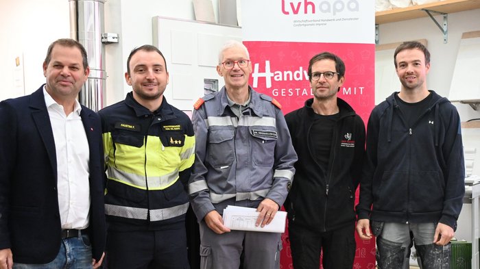 RISCALDAMENTO SICURO Cinque uomini in abbigliamento da lavoro e vigile del fuoco davanti a uno striscione LVH