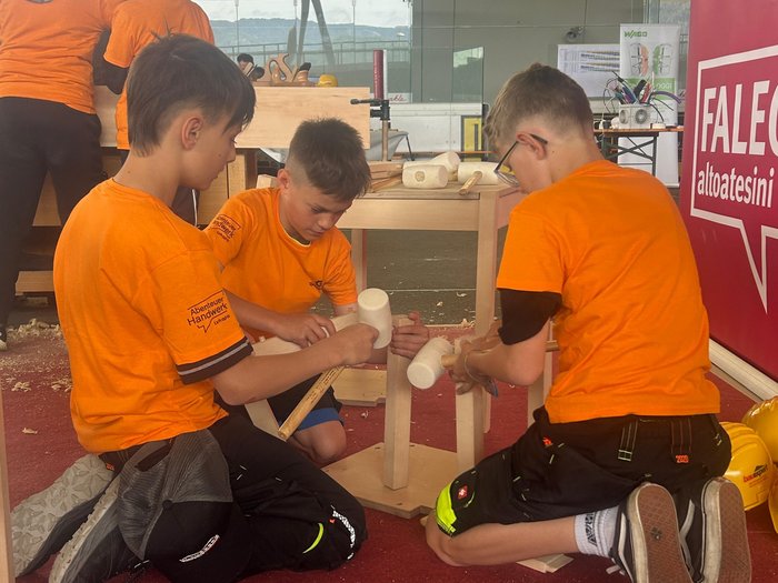 Nachwuchsinitiative „Abenteuer Handwerk“ der Intercable Arena Kinder arbeiten gemeinsam an einem Holzprojekt in orangefarbenen T-Shirts