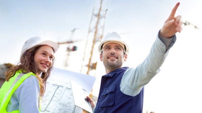 BUILD IT! Modernes Bauen in Südtirol Ingenieure mit Bauplänen auf Baustelle mit Kränen im Hintergrund