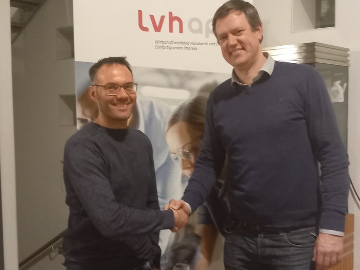 Neuer lvh-Ortsausschuss in Sexten Zwei Männer schütteln sich vor einem LVH-Banner die Hand in einem Innenraum