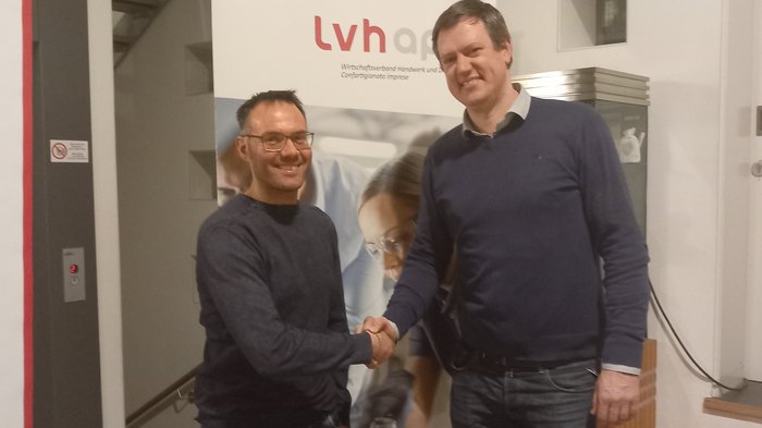 Neuer lvh-Ortsausschuss in Sexten Zwei Männer schütteln sich vor einem LVH-Banner die Hand in einem Innenraum
