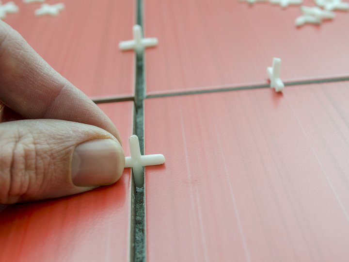 Fliesen-, Platten- und Mosaikleger Hand platziert Fliesenkreuze zwischen roten Bodenfliesen