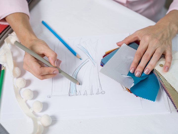 Tapezierer - Raumausstatter Hand zeichnet Modedesign und hält Stoffmuster in verschiedenen Farben