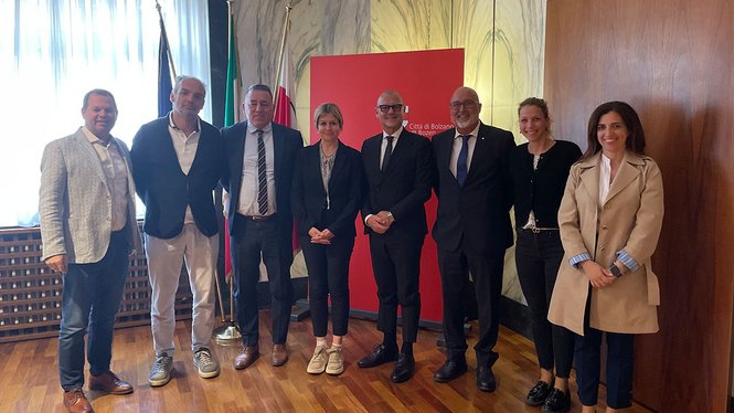 Gruppenfoto von acht Personen vor Fahnen und rotem Stadt Bozen Schild