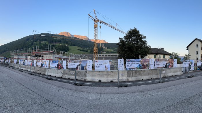Jugend motivieren! Baugelände mit Plakaten und Kran vor Berglandschaft in einem Dorf