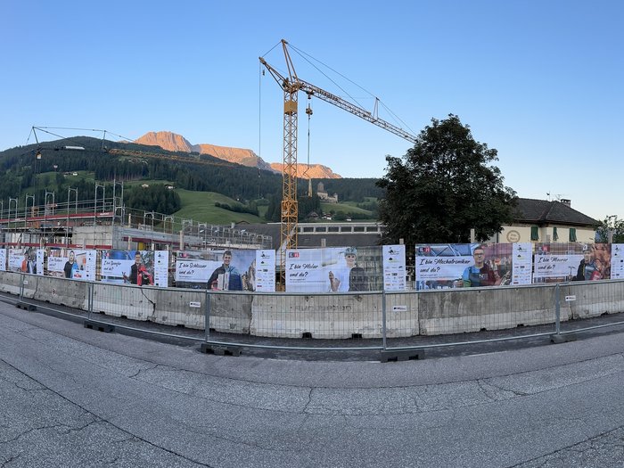 Jugend motivieren! Baugelände mit Plakaten und Kran vor Berglandschaft in einem Dorf