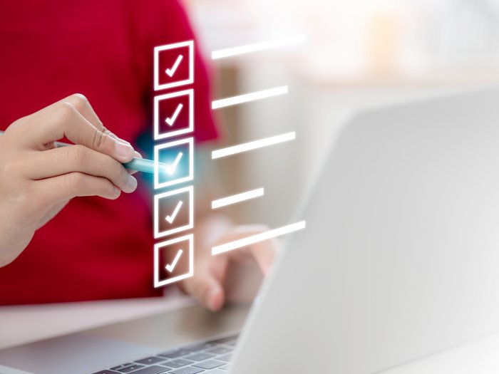 Ihre Meinung zählt: Grundlage für ein neues Ausbildungskonzept im Handwerk Hand markiert Punkte auf digitaler Checkliste vor Laptop