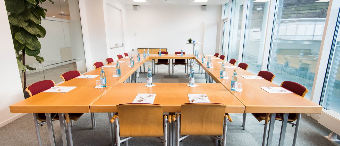 Vermietung Seminarräume Konferenzraum mit U-förmigen Tischen, Stühlen und Wasserflaschen an jedem Platz
