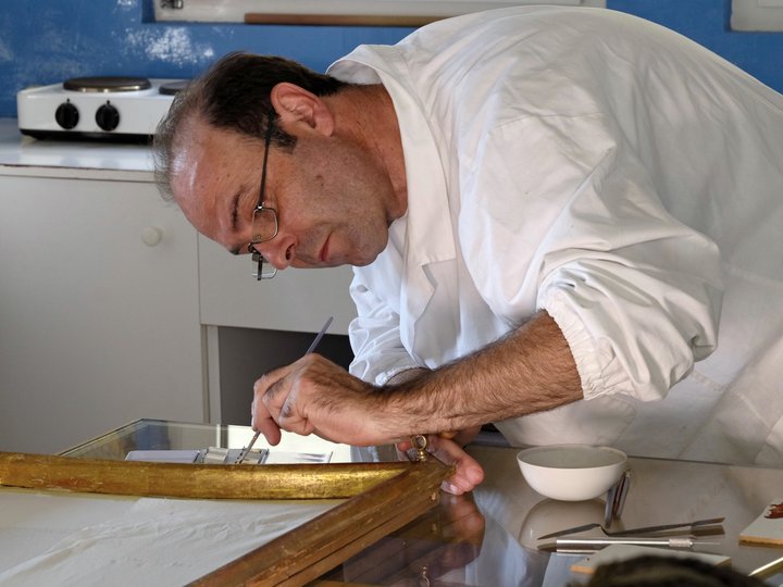 Restauratori Uomo con camice bianco restaura una cornice dorata