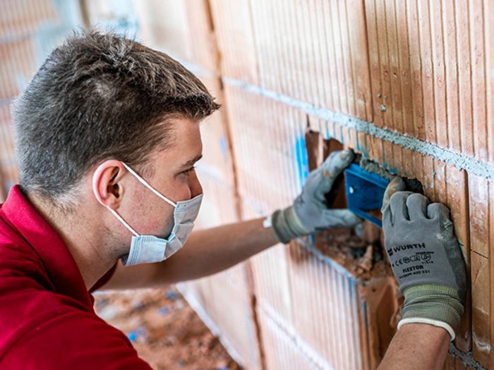 lvh und STA setzen auf lokale Betriebe Handwerker mit Maske und Handschuhen installiert eine elektrische Dose in einer Ziegelwand