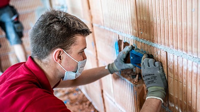 lvh und STA setzen auf lokale Betriebe Handwerker mit Maske und Handschuhen installiert eine elektrische Dose in einer Ziegelwand