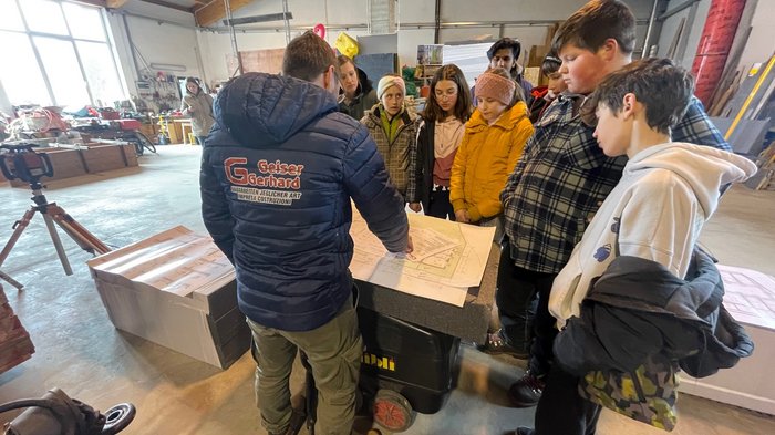 Jugendliche entdecken Berufe im Handwerk und Gastgewerbe Gruppe von Jugendlichen, die in einer Werkstatt Baupläne betrachten