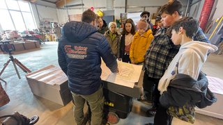 News Gruppe von Jugendlichen, die in einer Werkstatt Baupläne betrachten