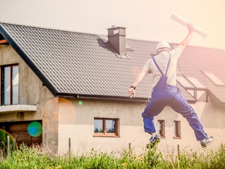 Informationen und Beratungen Bauarbeiter springt vor einem Haus mit Plänen in der Hand