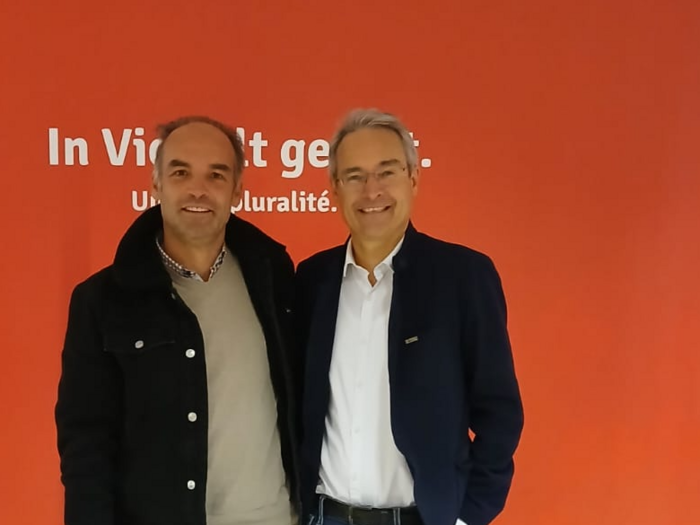 Treffen mit Dieter Steger: Herausforderung Berufsführerschein Zwei Männer lächeln vor rotem Hintergrund mit Text in Deutsch und Französisch