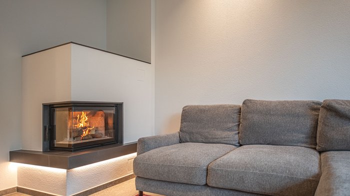 Information und Prävention Moderner Wohnzimmerbereich mit grauem Sofa und eingebautem Kamin mit Feuer