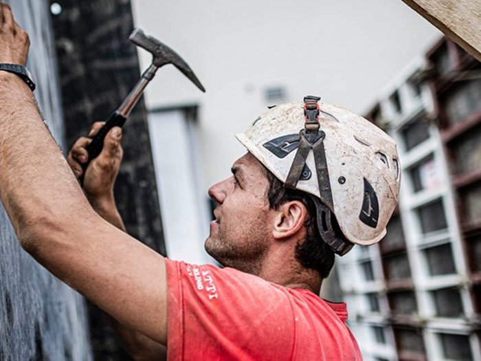 Südtirols Baubranche: „Uns steht die Krise noch bevor“ Bauarbeiter mit Helm hämmert an Wand bei Baustelle