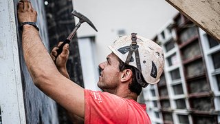 News Bauarbeiter mit Helm hämmert an Wand bei Baustelle